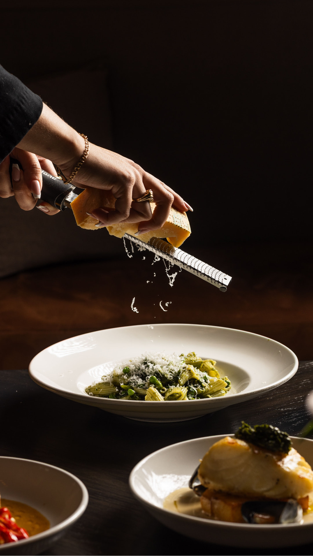 Parmesan grated over green pasta in low warm light